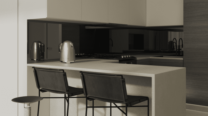 Une cuisine de villa moderne à Dubaï avec un design minimaliste, comprenant un îlot avec deux chaises noires et des appareils électroménagers en acier inoxydable, dont une bouilloire. Les tons neutres dominent la palette de couleurs.