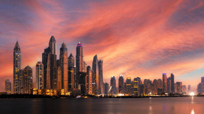 Une ligne d'horizon à couper le souffle de Dubaï avec de nombreux gratte-ciels illuminés sous un ciel coucher de soleil vibrant avec des nuages tourbillonnants roses et oranges.