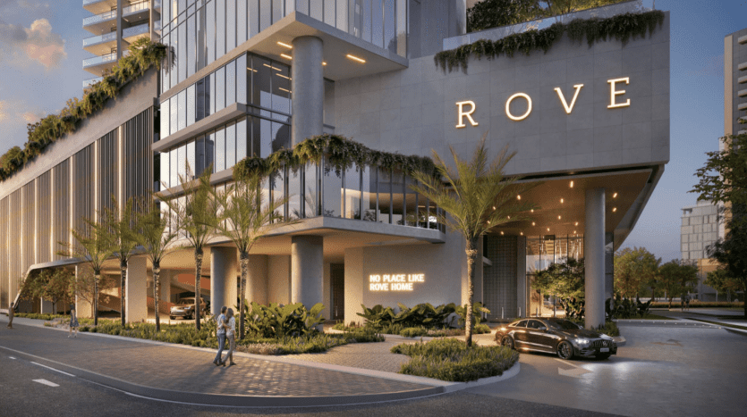 Extérieur d'un hôtel moderne au crépuscule avec une signalisation lumineuse indiquant « ROVE », une végétation luxuriante, une voiture à l'entrée et deux personnes marchant à Dubaï.