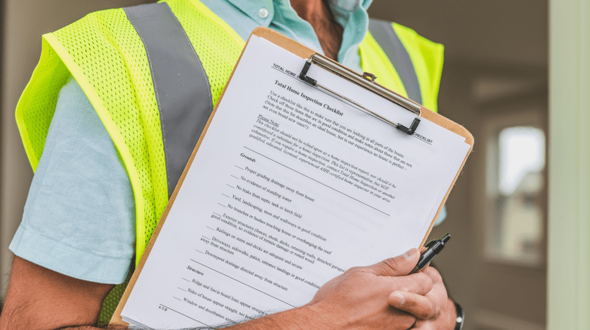 Un ouvrier du bâtiment vêtu d'un gilet jaune haute visibilité tenant un presse-papiers avec une liste de contrôle et un stylo appartement Dubaï, se concentrant sur le document, partiellement recadré ne montrant que le torse et les mains.