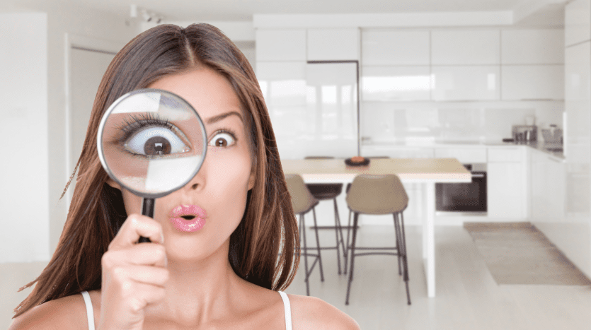 Une femme surprise tenant une loupe près d'un œil, ce qui agrandit considérablement son œil, dans une cuisine moderne d'une villa à Dubaï.