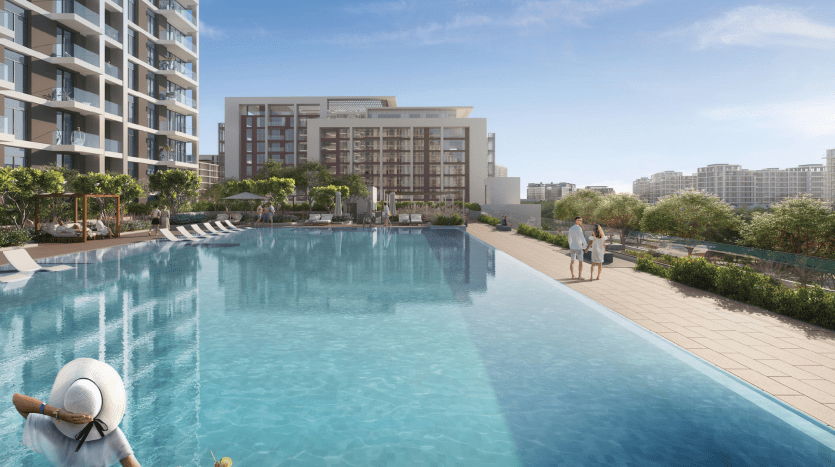 Une luxueuse piscine extérieure entourée d'immeubles de grande hauteur, de chaises longues et d'une verdure luxuriante, avec des gens profitant d'une journée ensoleillée dans un développement immobilier de Dubaï.