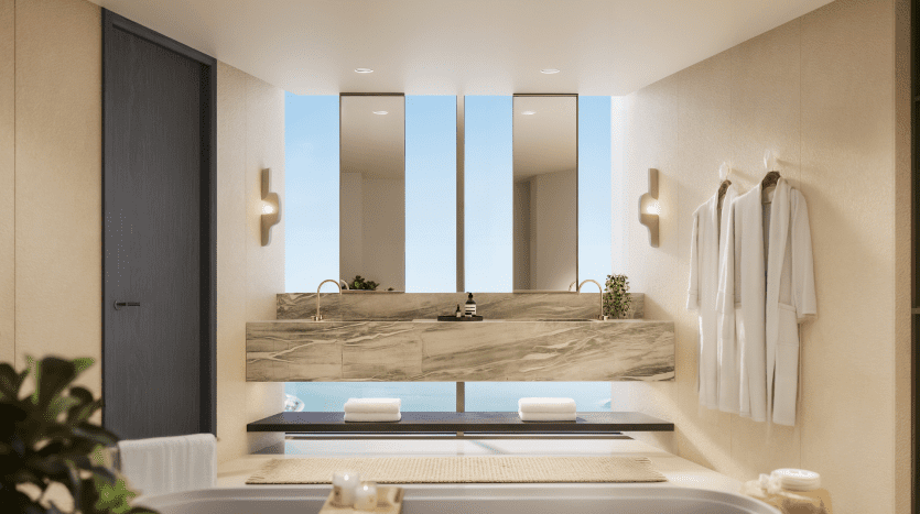 Une salle de bains moderne dans un appartement de Dubaï avec un grand miroir au-dessus d'un lavabo en marbre, flanqué de fenêtres verticales. Une baignoire luxueuse est visible au premier plan, avec des plantes et un éclairage doux renforçant l'ambiance sereine.