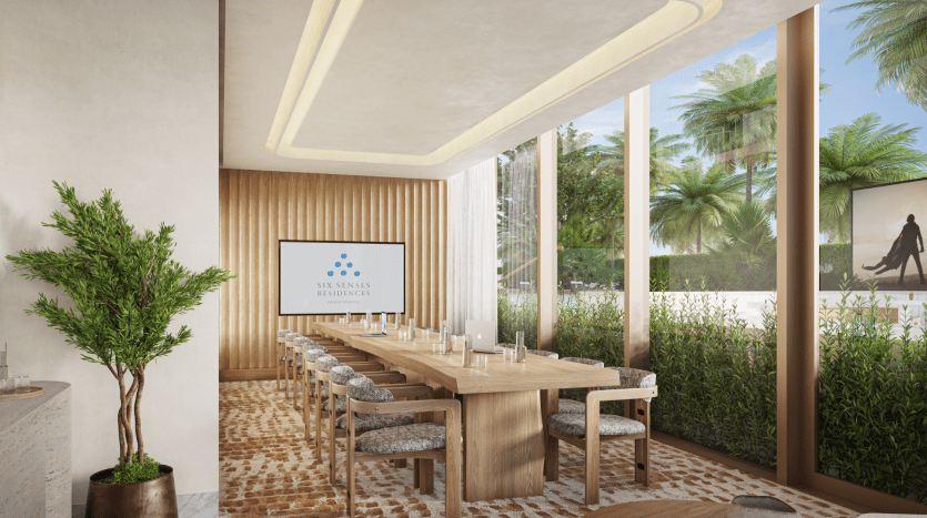 Salle de réunion moderne avec une grande table en bois, entourée de chaises moelleuses. Une bannière indiquant « Six Senses Residences » sur la gauche, de grandes fenêtres laissant apparaître une verdure luxuriante et un design intérieur élégant typique de l'immobilier Dubaï.