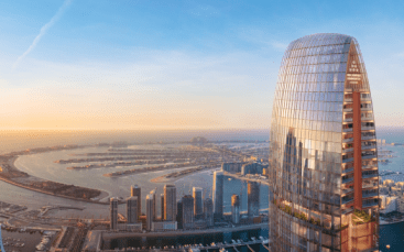 Vista aérea de una ciudad moderna al amanecer, con un rascacielos curvo en primer plano que domina una zona costera con una serie de islas artificiales cerca de Dubai.