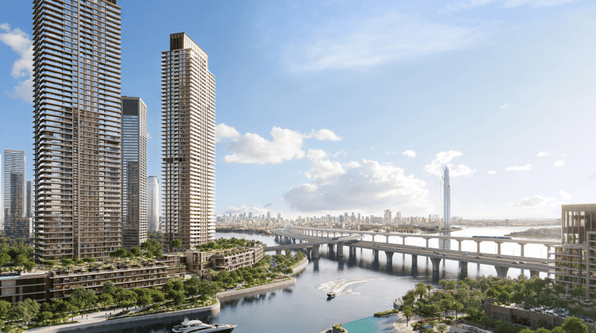 Un paysage urbain animé avec de grands gratte-ciel modernes au port Arlo Dubai Creek surplombe une rivière animée de bateaux. Un élégant pont enjambe l'eau, reliant des espaces verts luxuriants des deux côtés sous un ciel bleu partiellement nuageux. L’horizon lointain d’un autre développement d’Emaar est visible à l’horizon.