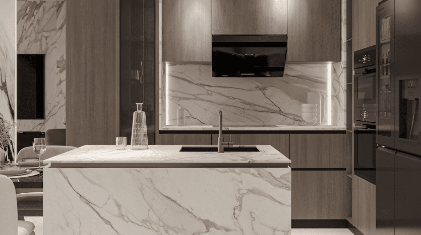Une cuisine moderne du Primero Residences Al Furjan comprend un îlot en marbre avec un évier intégré et un robinet minimaliste. La pièce est ornée d'armoires en bois, d'un éclairage zénithal et d'une élégante hotte noire. Les appareils électroménagers, notamment un four et un réfrigérateur, sont parfaitement intégrés aux armoires.