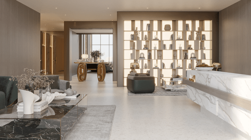 Un espace de vie moderne du Primero Residences Al Furjan présente des accents de marbre, une étagère rétroéclairée avec des œuvres d'art, des canapés gris et une table basse en verre avec des objets décoratifs. Une porte mène à une pièce ensoleillée avec de grandes fenêtres et des tables en bois uniques, tandis que les plantes renforcent l'atmosphère sereine.