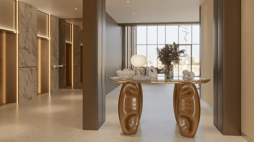Un couloir moderne et élégant avec des accents de marbre et un éclairage tamisé dans les résidences Primero Al Furjan. Au centre se trouve une console sophistiquée avec des pieds dorés sculpturaux uniques, ornés d'objets décoratifs et d'un bouquet de fleurs. De grandes fenêtres au fond offrent une vue sur le paysage urbain.