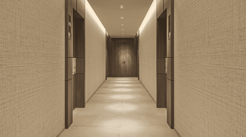 Un couloir moderne et bien éclairé du Primero Residences Al Furjan avec des murs texturés beiges et du carrelage au sol. Il y a des portes des deux côtés menant aux pièces, et le couloir se prolonge vers une seule porte au bout, créant une sensation de profondeur et de symétrie.
