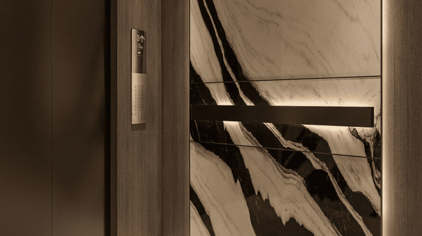 L'intérieur d'un ascenseur élégant et moderne du Primero Residences Al Furjan présente des boiseries sombres et un mur d'accent en marbre poli avec des veines noires et blanches. Un panneau de commande éclairé et futuriste avec un clavier et un affichage numérique est visible sur le côté gauche de la porte de l'ascenseur.