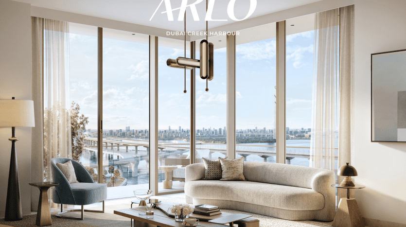 Un salon moderne avec de grandes fenêtres offrant une vue sur le port de Dubai Creek. La pièce comprend un canapé incurvé beige, une chaise bleue, une table basse, un lampadaire et un luminaire mural. Le texte en haut indique « ARLO - Emaar's Dubai Creek Harbour ».