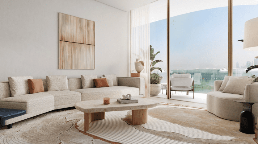 Un salon moderne des Dubai Harbour Residences avec de grandes fenêtres donnant sur le front de mer. Il comprend un canapé sectionnel beige clair avec des coussins de couleur rouille, un fauteuil rond, une table basse en bois, des œuvres d'art murales abstraites, des plantes en pot et un tapis aux tons neutres avec un motif ondulé.