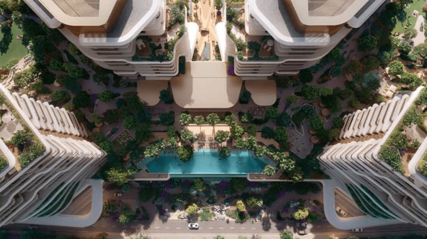 Vue aérienne d'un complexe résidentiel moderne de plusieurs étages avec un aménagement paysager verdoyant. Les bâtiments sont disposés symétriquement autour d'une cour centrale dotée d'une grande piscine, entourée d'arbres et d'allées. Une route longe le devant du complexe Verdes.