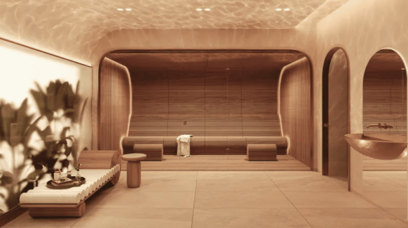 Salle de spa luxueuse à l'ambiance sereine, dotée d'un éclairage doux et chaleureux et d'accents en bois. La pièce comprend une chaise longue rembourrée, un banc en bois, une grande plante en pot avec des feuilles vertes verdoyantes, un évier élégant et des arches décoratives. Une serviette blanche roulée repose sur un banc.
