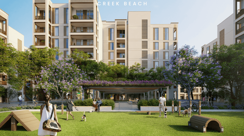 Un complexe résidentiel moderne composé de plusieurs bâtiments de taille moyenne entoure un parc verdoyant. Les gens promènent des chiens, utilisent l'équipement d'agilité pour chiens et sont assis sur des bancs sous une pergola couverte de plantes à fleurs violettes. Les arbres et la verdure abondent, créant une oasis rappelant une lande sereine.