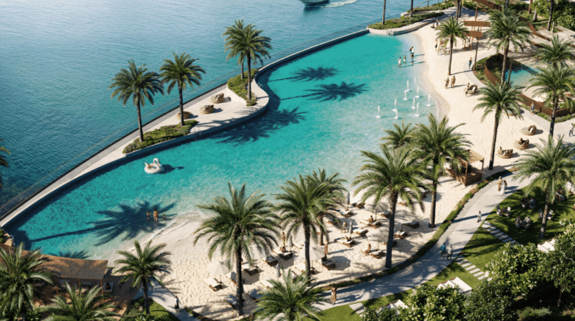 Aerial view of Adress Residences, a luxurious tropical complex featuring a large curved pool with fountains, surrounded by palm trees and sandy areas with sun loungers. A few people are enjoying the pool, and part of the picturesque ocean is visible in the background.