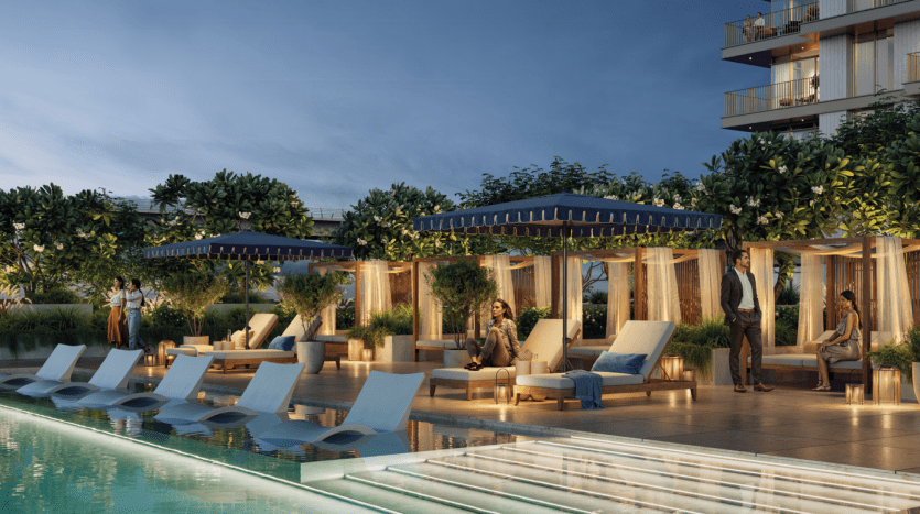 At dusk, a luxurious rooftop pool at the Address Residences features cabanas with curtains, sun loungers and lush vegetation. Several people relax on the sun loungers and in the cabanas. The scene is softly lit, creating a calm, elegant ambience.