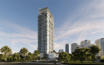 Le gratte-ciel moderne et de grande hauteur connu sous le nom de Skyhills 2 arbore une façade en verre saisissante, se dressant fièrement sur un ciel partiellement nuageux. Entouré de palmiers et d'une végétation luxuriante, il domine des bâtiments plus petits tandis que quelques voitures passent sur la route en face.