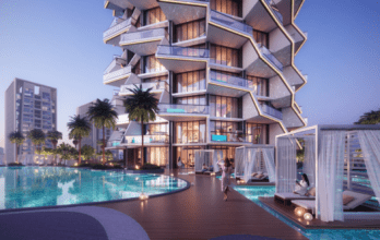 Binghatti Royale, a luxurious and modern high-rise building, features a unique geometric architecture. In front of it, there is a serene swimming pool surrounded by palm trees and cabanas. A person in a purple dress walks by the pool, while another person relaxes inside a cabana with flowing curtains.