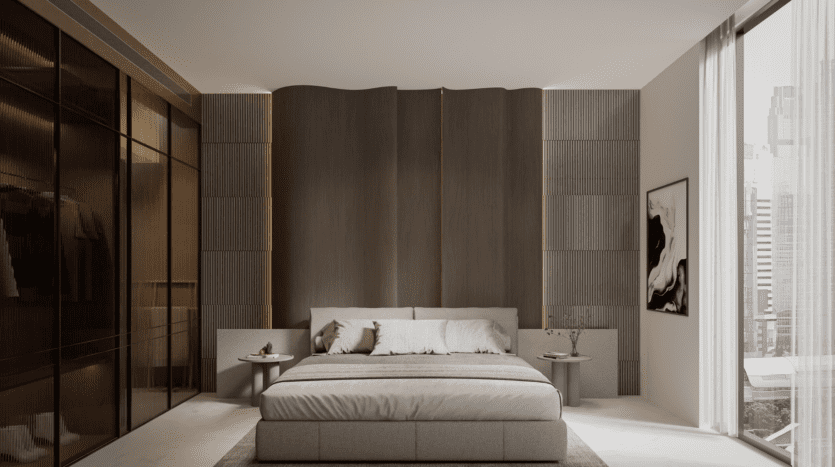 Dans une chambre moderne du One Beverly Dubai, un grand lit est centré contre un mur de tête de lit en bois texturé. Flanqué de tables d'appoint rondes, il fait face à des baies vitrées du sol au plafond avec vue sur la ville. Une œuvre d'art encadrée minimaliste est accrochée sur le mur de droite, avec une armoire sur la gauche.