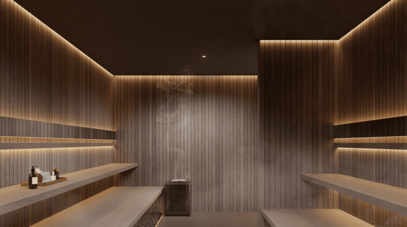 L'intérieur du sauna One Beverly Dubai est doté de bancs et de murs en bois modernes, d'un éclairage d'ambiance doux et de vapeur provenant d'un poêle central en pierre. Plusieurs petites bouteilles et serviettes sont soigneusement disposées sur le banc, offrant une évasion sereine.