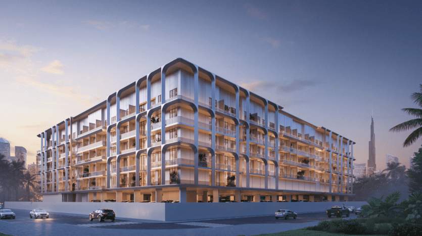 Un immeuble résidentiel moderne à plusieurs étages avec une façade incurvée unique dans un cadre urbain au coucher du soleil. Des palmiers bordent la rue près du One Bervely Dubai, et quelques voitures sont garées à proximité. Une haute silhouette de la ville est visible en arrière-plan.