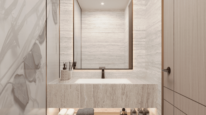 Une salle de bains moderne du One Beverly Dubai est dotée d'un grand miroir au-dessus d'une vanité en pierre grise. Le plan de travail contient des articles de toilette tels que des brosses à dents et des bouteilles. Un éclairage doux et des luminaires élégants créent une atmosphère minimaliste et élégante.