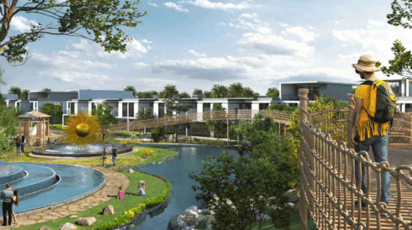 Vue panoramique d'un parc luxuriant à Sun City, avec une voie navigable sinueuse, des passerelles et des villas modernes en arrière-plan. Les visiteurs profitent de la journée ensoleillée, avec une personne debout sur un pont portant un chapeau et un sac à dos, surplombant le paysage.