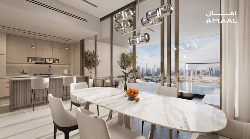 La salle à manger Amaal 8 présente un design moderne avec une grande table en marbre, des chaises blanches et un éclairage suspendu élégant. Une cuisine ouverte avec des armoires en bois orne l'arrière-plan, tandis que des baies vitrées présentent un superbe panorama urbain. Un bol d'oranges ajoute une touche de couleur à la table.