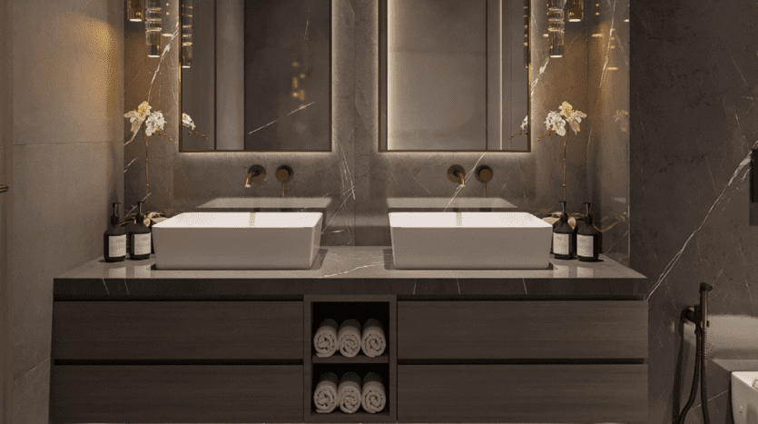 Une salle de bains moderne à One Park Square dispose d'un meuble-lavabo double avec des vasques blanches épurées et des robinets en bronze. Deux miroirs sont suspendus au-dessus, encadrés par un éclairage doux. Des orchidées et des produits de toilette en bouteille ornent le comptoir, avec des serviettes roulées soigneusement rangées en dessous.