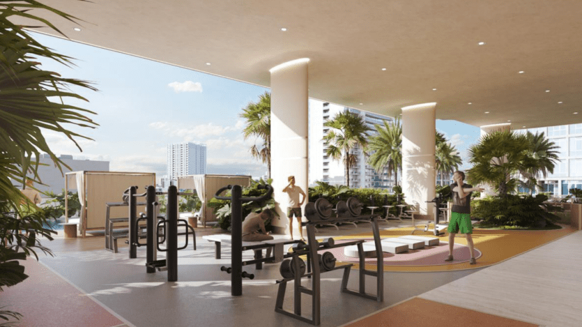 Au One Park Square, l'espace fitness en plein air regorge d'activité, les gens soulevant des poids et faisant de l'exercice sur des bancs au milieu de plantes tropicales luxuriantes. Les bâtiments se dressent en arrière-plan sous un ciel dégagé, ajoutant une touche urbaine à cet espace de gym en plein air dynamique.
