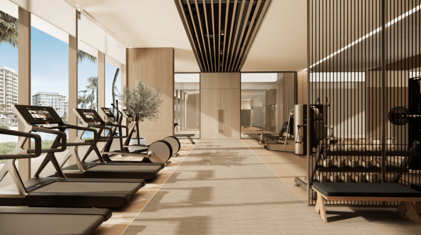 La salle de sport moderne de Bay Grove Residences dispose de grandes fenêtres offrant une vue sur les palmiers et les bâtiments. Équipé de tapis de course, d'appareils d'exercice et de poids libres, l'espace associe des panneaux de bois clair à des éléments de design épurés pour une atmosphère spacieuse et accueillante.