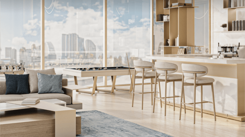 Un espace de vie moderne et lumineux de la collection Cove Edition 2 avec de grandes fenêtres présentant un paysage urbain. La pièce comprend un baby-foot, un coin bar avec des tabourets, un canapé gris confortable et une table basse en bois sur un tapis bleu clair. La décoration est minimaliste avec une palette de couleurs neutres.