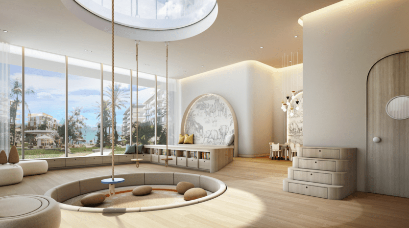La salle de jeux moderne pour enfants du Bay Grove Residences comprend une aire de jeux circulaire encastrée avec une balançoire en bois et des sièges moelleux. De grandes fenêtres révèlent une vue panoramique sur les palmiers et l'océan, tandis que la pièce est lumineuse avec du parquet en bois clair et une décoration ludique.