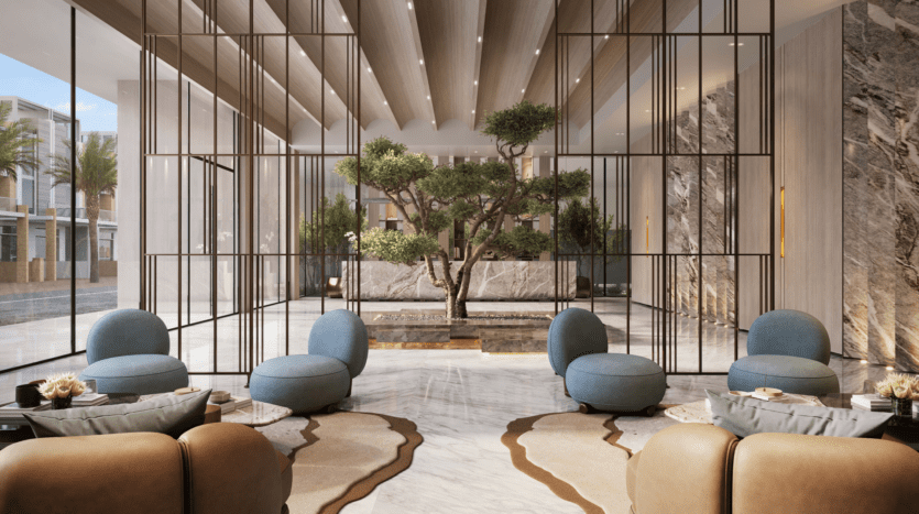 Un hall d'hôtel moderne avec un sol en marbre élégant et de grands panneaux en verre. Des sièges rembourrés bleus et marron entourent une zone centrale avec un arbre et des plantes. La lumière naturelle pénètre par de grandes fenêtres, créant une atmosphère lumineuse et accueillante.