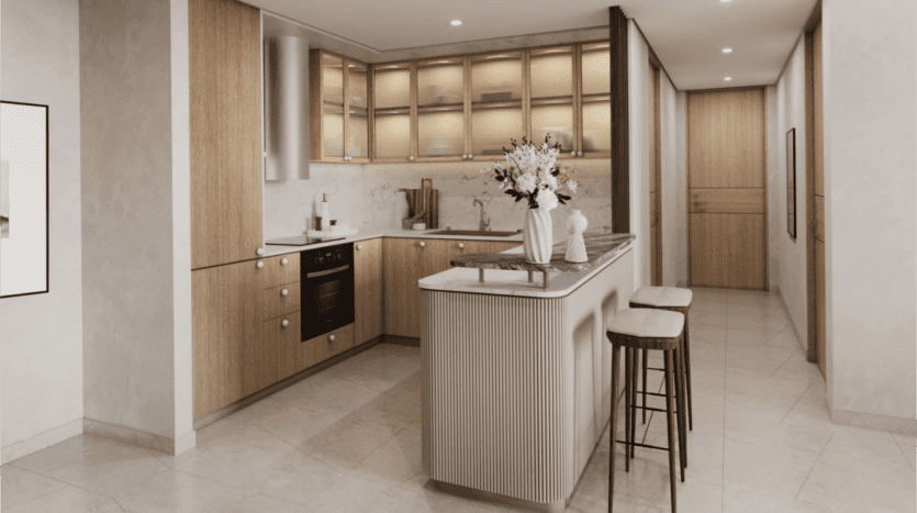 Intérieur de cuisine moderne avec armoires en bois Saria et comptoir en marbre. La pièce comprend un îlot avec deux tabourets de bar, des appareils électroménagers en acier inoxydable et une composition florale. Elle est bien éclairée avec un éclairage encastré et une palette de couleurs neutres.