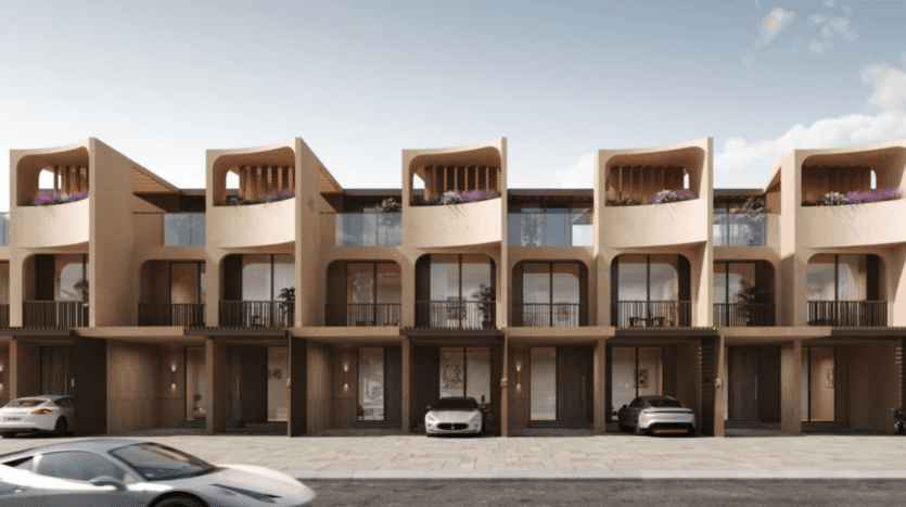 Une rangée de maisons de ville modernes de trois étages aux couleurs beiges, avec des arcades incurvées et des balcons uniques rappelant les jardins de Kensington. Chaque unité dispose d'un garage et d'une petite allée avec des voitures garées, le tout sur fond de ciel bleu vif de Dubaï.