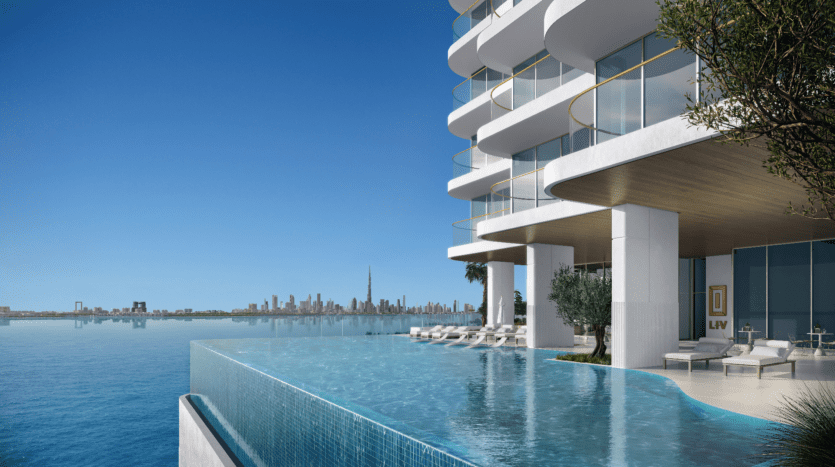 LIV Maritime présente un immeuble résidentiel luxueux avec une piscine à débordement moderne surplombant un vaste plan d'eau. L'horizon d'une ville avec de hauts gratte-ciels orne l'arrière-plan sous un ciel bleu clair, offrant un mélange inégalé de tranquillité et de sophistication urbaine.