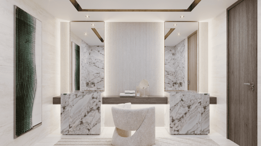 Une salle de bains moderne et élégante au style maritime LIV comprend une double vasque en marbre avec de grands miroirs et une chaise blanche élégante. Les murs sont décorés d'un motif texturé et d'une œuvre d'art abstraite verte. Un éclairage doux crée une ambiance chaleureuse et accueillante.