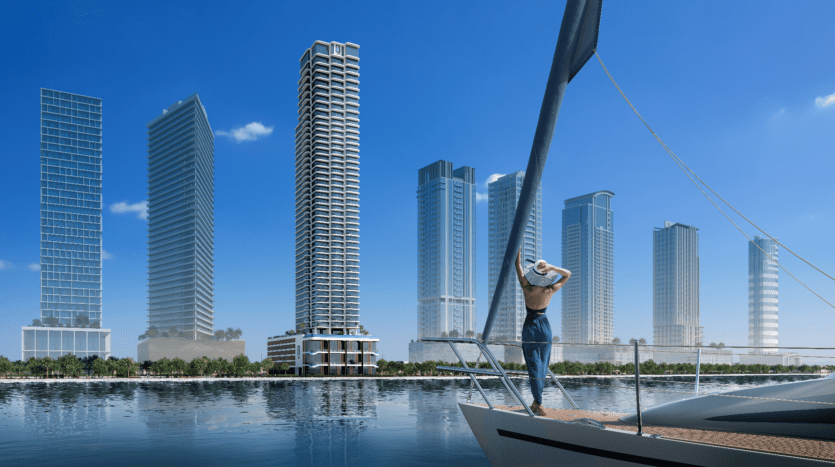 Une personne se tient debout sur un yacht de LIV Maritime, contemplant l'horizon d'une ville moderne avec de hauts gratte-ciel. L'eau bleue calme reflète les bâtiments, créant une scène urbaine sereine sous le ciel clair.