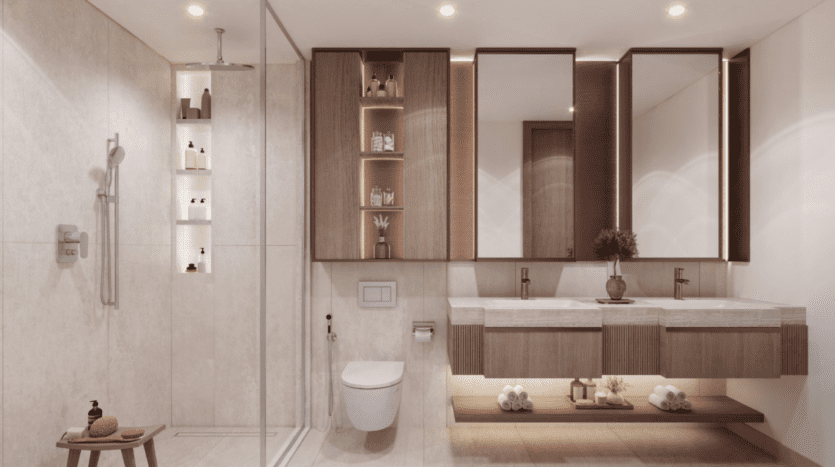 Le Hillgate dispose d'une salle de bains moderne avec une douche vitrée, des toilettes murales et un double lavabo. Des armoires en bois avec miroirs offrent du rangement, tandis que des étagères encastrées présentent des éléments de décoration. Un éclairage doux complète le design minimaliste aux tons neutres, créant une ambiance chaleureuse.