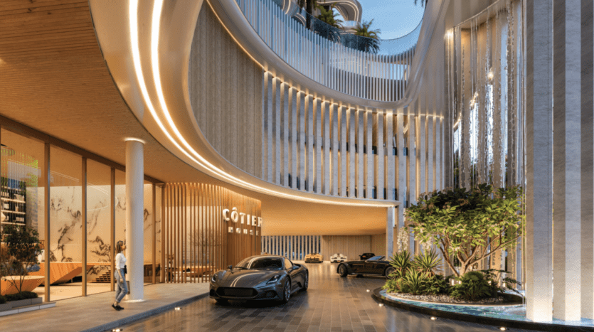 L'entrée de Cotier House respire le luxe avec son architecture épurée, sa façade incurvée et ses hautes fenêtres en verre. L'éclairage ambiant met en valeur deux voitures haut de gamme sur l'allée polie, entourée de verdure luxuriante et de jeux d'eau artistiques.