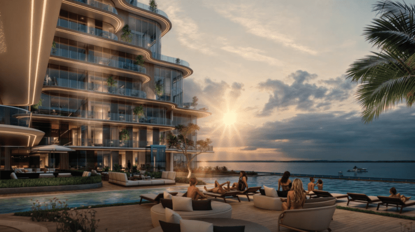 Le luxueux complexe d'appartements Cotier House au coucher du soleil bénéficie d'un design moderne avec des balcons incurvés. Les résidents se détendent sur la terrasse au bord de la piscine, savourant la vue sur l'océan et un bateau au loin sous un ciel partiellement nuageux. Des palmiers et une végétation luxuriante rehaussent le paysage pittoresque.