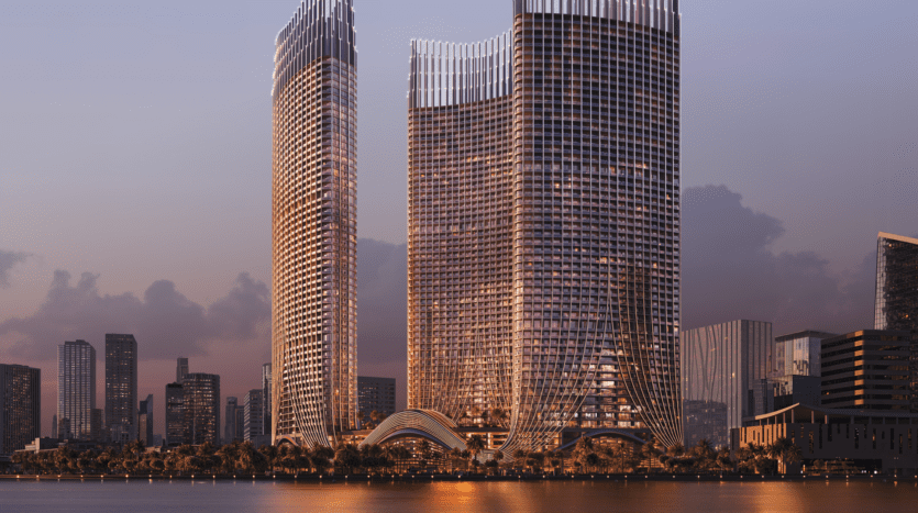Un paysage urbain époustouflant au crépuscule présente des gratte-ciel modernes aux conceptions architecturales uniques, leurs reflets scintillant sur un front de mer calme, sous un ciel partiellement nuageux illuminé par la lueur chaleureuse et ambiante des lumières de la ville.