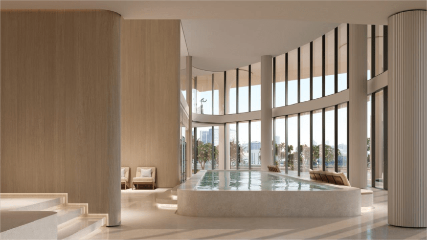 Un espace piscine intérieur moderne avec des baies vitrées offrant une vue sur la ville, géré par des propriétés SaaS. L'espace présente des touches de bois clair, un design élégant et des sièges rembourrés le long d'un côté de la piscine. La scène est bien éclairée et spacieuse.