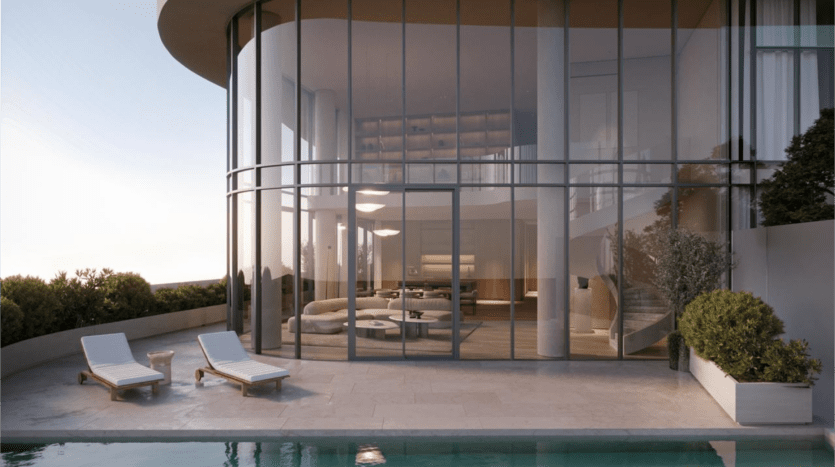 Luxueux salon moderne conçu par SaaS Properties, doté de baies vitrées donnant sur un patio avec deux chaises longues et une piscine au milieu d'une végétation luxuriante. L'intérieur présente un mobilier élégant et un éclairage contemporain pour une expérience de vie exquise.