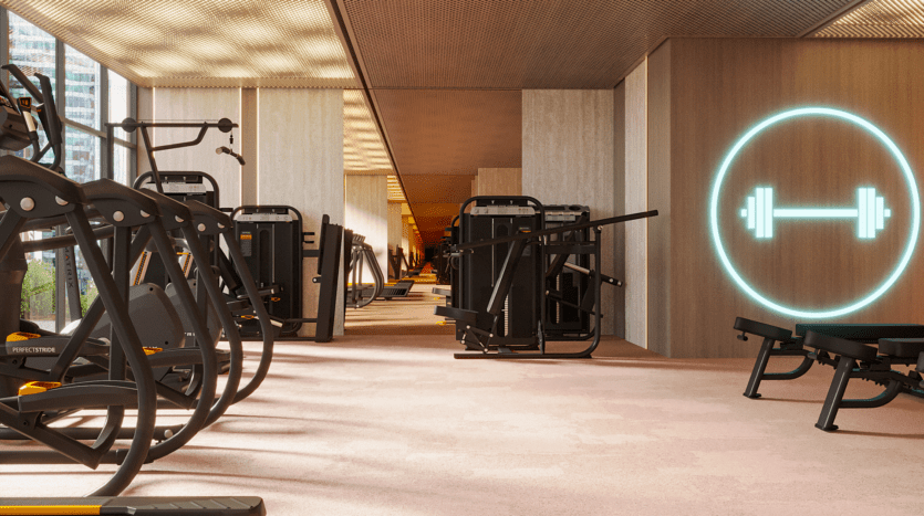 Un intérieur de salle de sport moderne avec divers appareils d'exercice et bancs alignés le long des murs. Une icône d'haltère lumineuse orne un panneau en bois et de grandes fenêtres offrent une vue sur les bâtiments de la ville. L'espace est bien éclairé et spacieux.