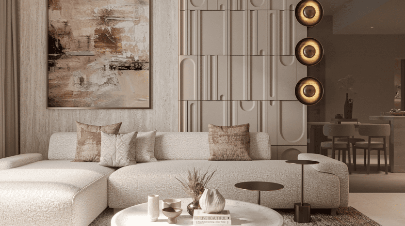 Un salon moderne comprend un grand canapé d'angle beige avec des coussins à motifs, une table basse ronde avec des objets décoratifs et des œuvres d'art abstraites sur le mur. Des appliques murales circulaires fournissent un éclairage chaleureux et un coin cuisine est visible en arrière-plan.