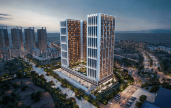 Aerial view of Binghatti's latest modern urban development with two tall skyscrapers illuminated at dusk. Surrounding these elite buildings are roads, green spaces and other skyscrapers under a twilight sky.